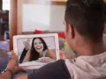 Un homme en relation à distance profite d'un appel vidéo avec sa compagne, dont le sourire illumine l'écran de sa tablette.
