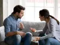 Un couple discute sur un canapé, les mains tendues, peut-être lors d'une séance de thérapie de couple pour améliorer leur communication.