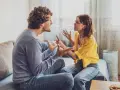 Un couple en plein conflit dans le salon, leurs visages tendus et leurs mains agitées témoignent d'une dispute animée.