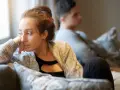 Une femme songeuse, le regard perdu, semble ressentir une profonde insécurité affective. Un homme est assis derrière elle, le dos tourné.