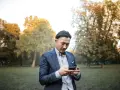 Un homme en costume, concentré sur son téléphone, dans un parc automnal. Une phrase provocante pour un homme pourrait être écrite sur son écran.
