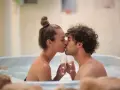 Un couple s'embrasse tendrement dans un jacuzzi, deux coupes de champagne à la main, pour un bain romantique inoubliable.