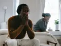 Un couple traverse une crise, visiblement préoccupés, assis séparément dans une chambre lumineuse.