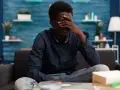 Un homme qui n'a pas confiance en lui, le visage caché dans la main, assis sur un canapé, l'air accablé.