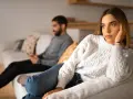 Un couple s'ennuie dans son couple, chacun absorbé par son téléphone sur le canapé, le regard perdu dans le vide.