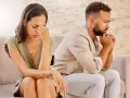 Un couple assis dos à dos, visiblement affecté par des disputes incessantes. La femme se tient la tête, l'air accablé, tandis que l'homme fixe le vide, les mains jointes.