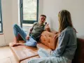 Un homme et une femme discutent sur un canapé en cuir marron. Leurs vêtements décontractés suggèrent un moment de détente, peut-être un double lien familial ou amical.