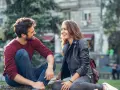 Un homme qui veut vous voir, assis sur l'herbe, rit avec une jeune femme. Ils semblent partager un moment complice et joyeux.