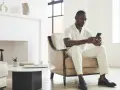 Un homme en tenue claire, assis dans un fauteuil, regarde son téléphone. Il attend un message, car il ne m'écrit plus comme avant.