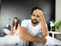 Un homme pensif sur un lit, sa compagne floue derrière. Comment attiser le désir d'un homme ? Peut-être par la communication et la connexion.