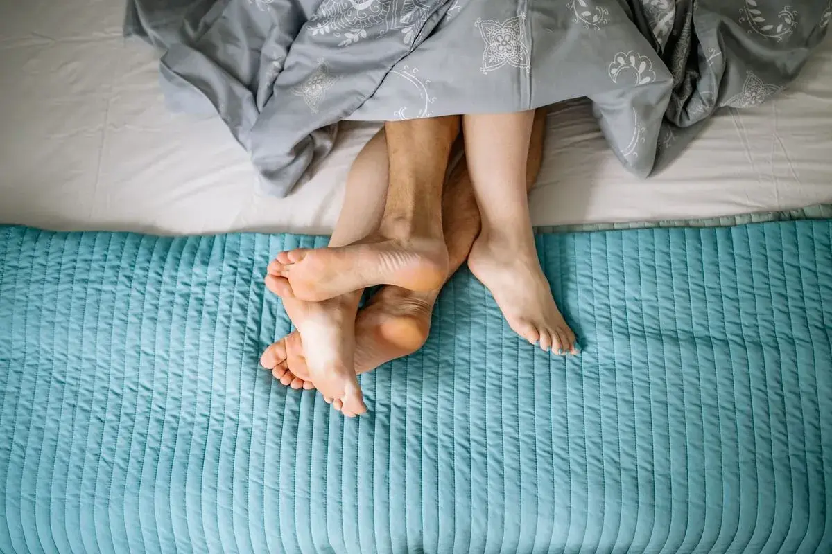 Pieds entrelacés sous une couette, évoquant la chaleur et la libido femme.