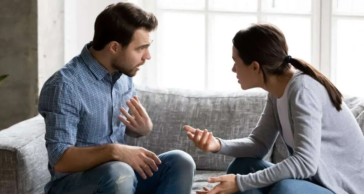 Un couple discute sur un canapé, les mains tendues, peut-être lors d'une séance de thérapie de couple pour améliorer leur communication.
