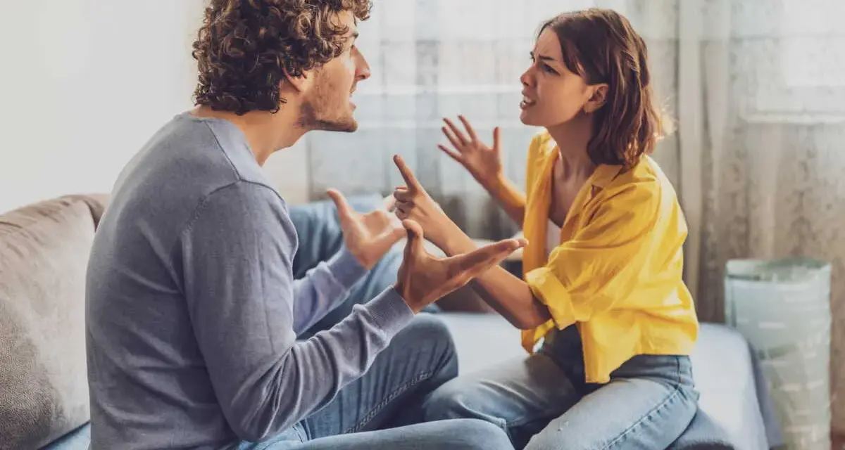 Un couple en plein conflit dans le salon, leurs visages tendus et leurs mains agitées témoignent d'une dispute animée.