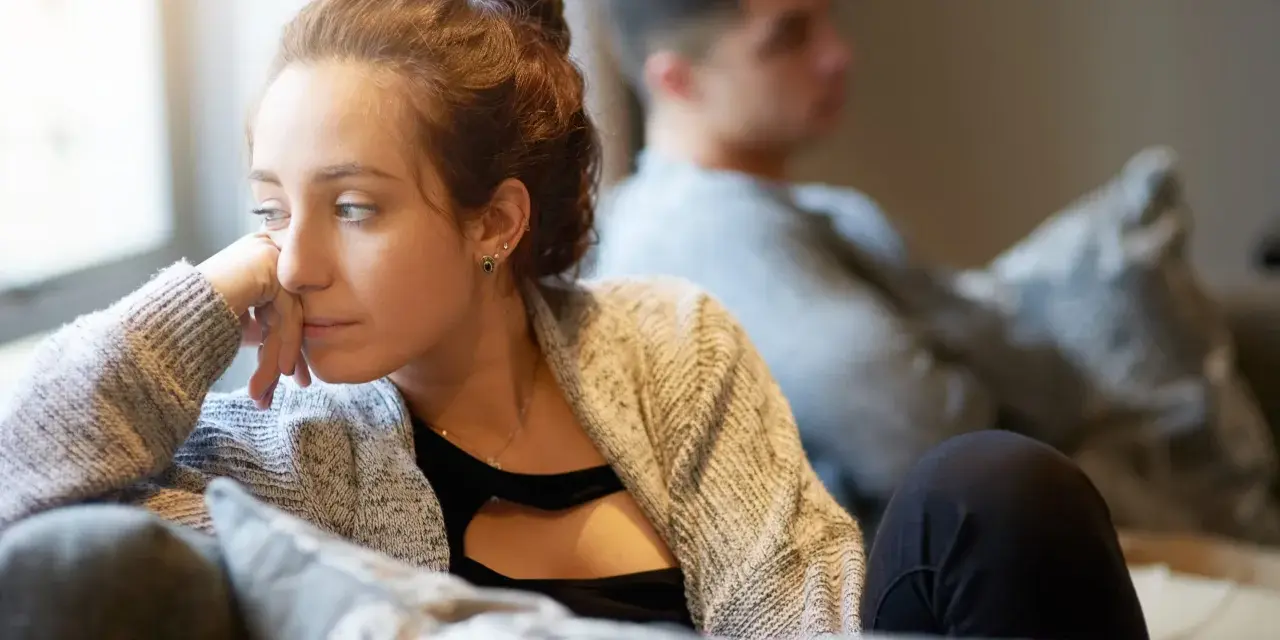Une femme songeuse, le regard perdu, semble ressentir une profonde insécurité affective. Un homme est assis derrière elle, le dos tourné.