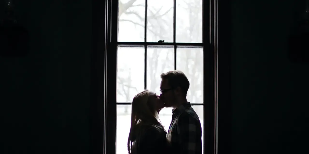 Silhouette d'un couple s'embrassant devant une fenêtre, une alchimie entre deux personnes capturée dans la lumière douce.
