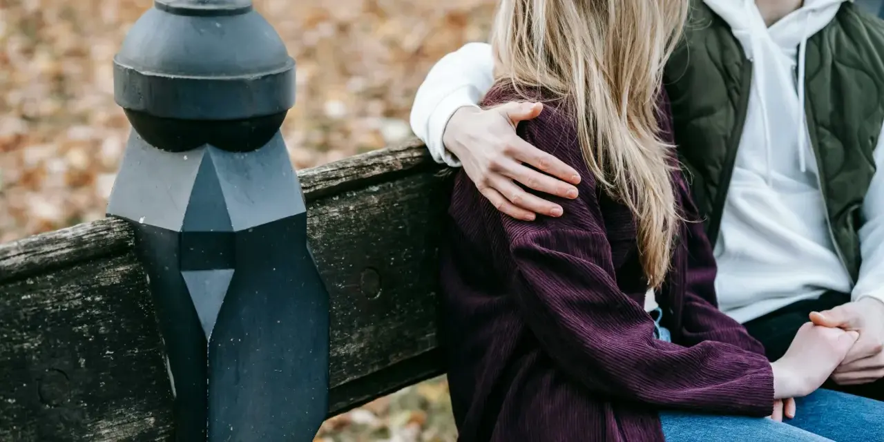 Un homme enlace tendrement une femme assise à ses côtés sur un banc. Un geste qui dit "comment dire je t'aime sans le dire".