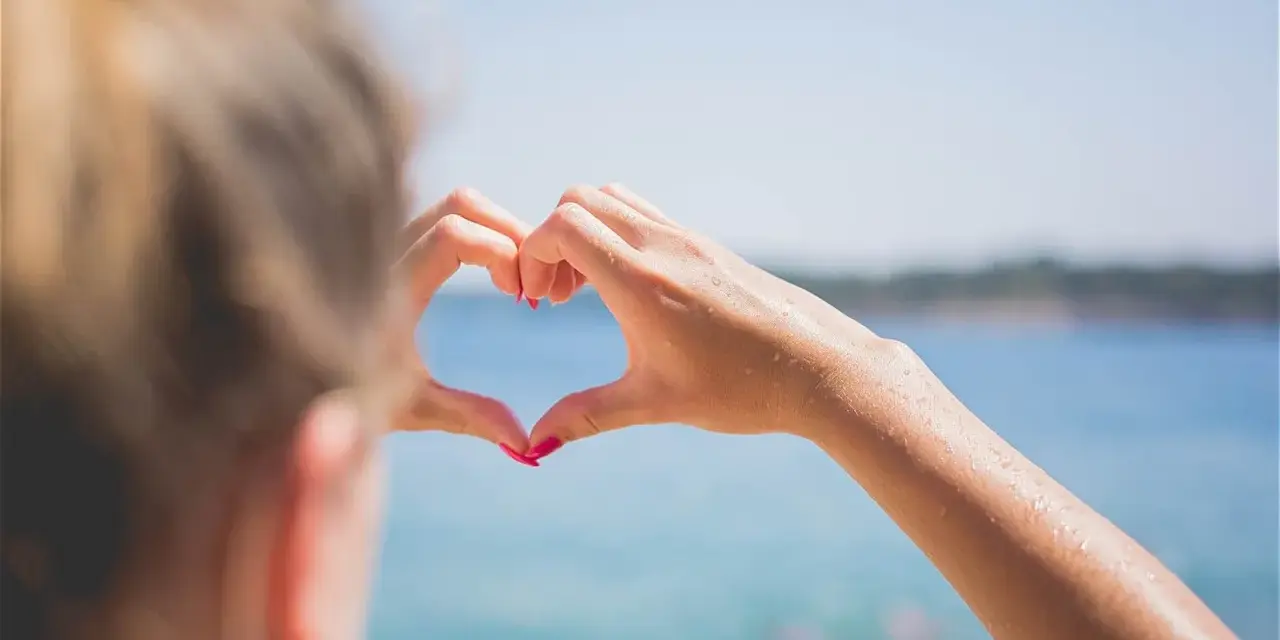 Message après premier rendez-vous avec un homme : un cœur formé par des mains mouillées sur fond de mer bleue.