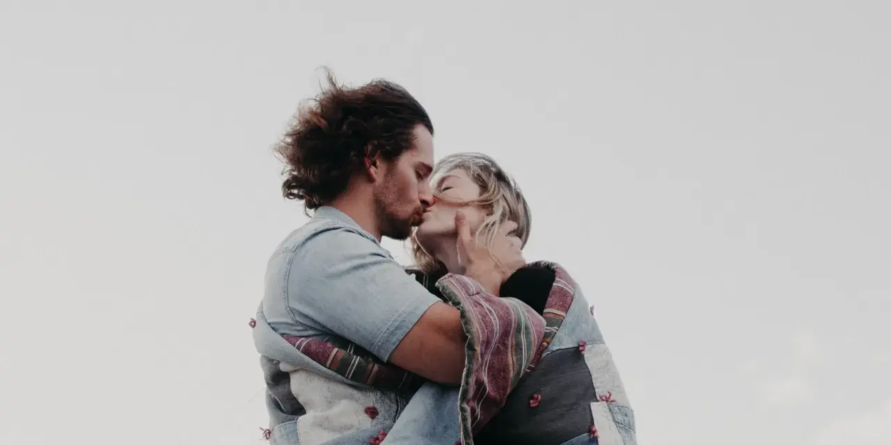 Un couple s'embrasse tendrement, enveloppé dans une couverture. Une belle illustration de comment trouver un mec et vivre un amour sincère.