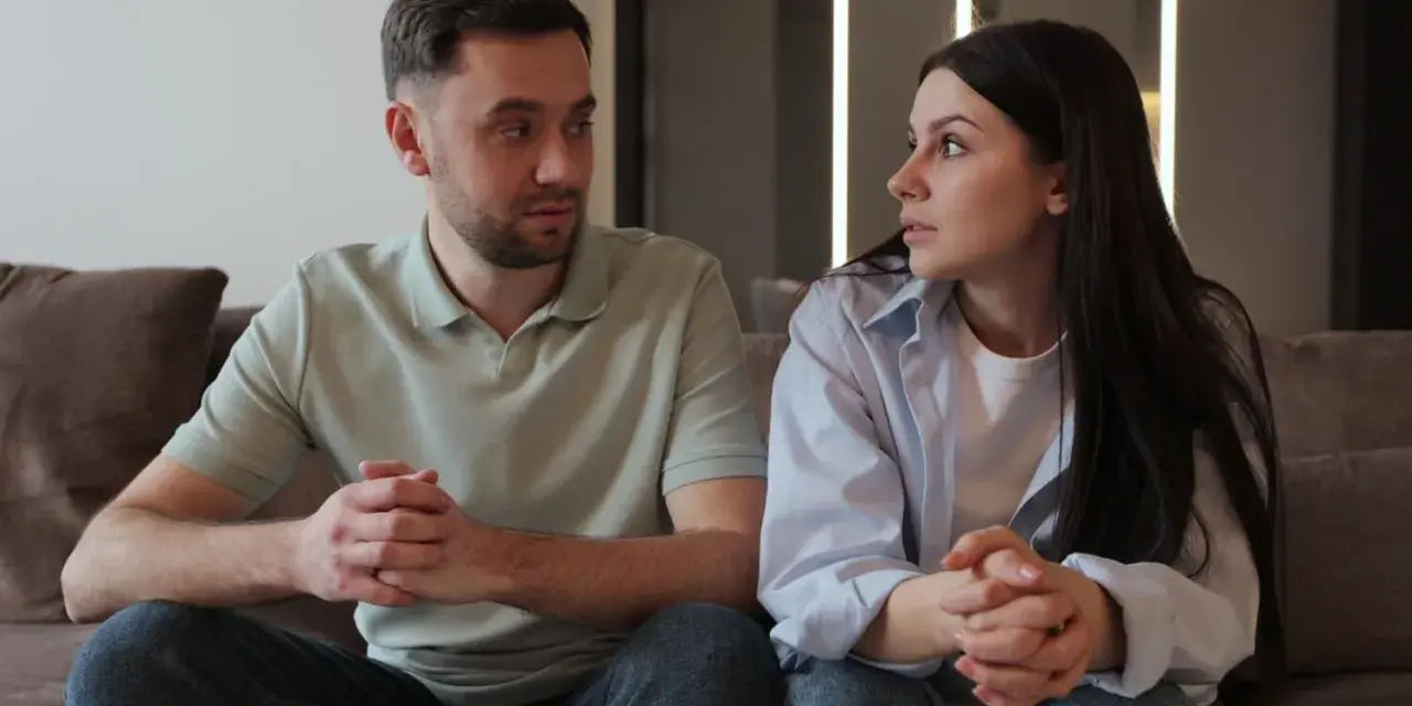 Un couple, peut-être un peu psycho, se regarde intensément, les mains jointes, sur un canapé.
