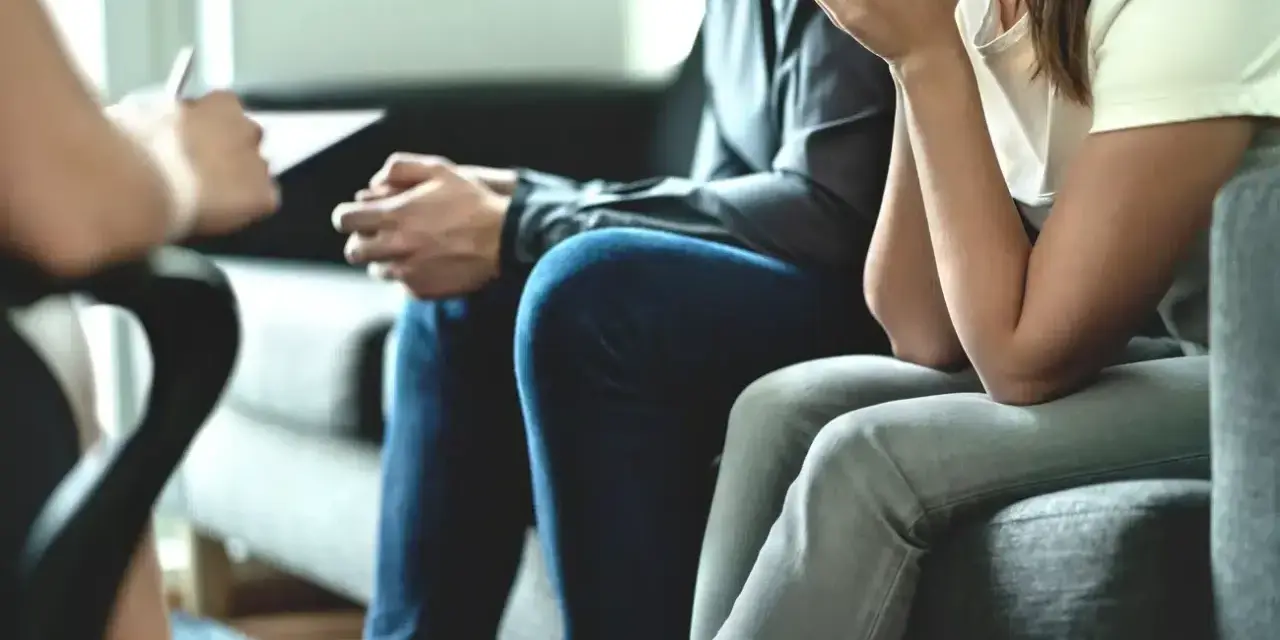 Un couple en pleine thérapie de couples, assis sur un canapé, échangeant avec un thérapeute.