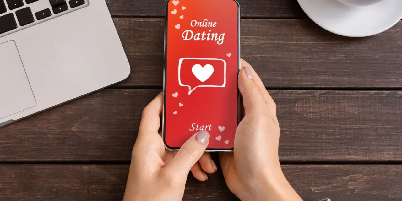 Une personne utilise une appli de rencontre sur son téléphone. L'écran affiche "Online Dating" avec un cœur.