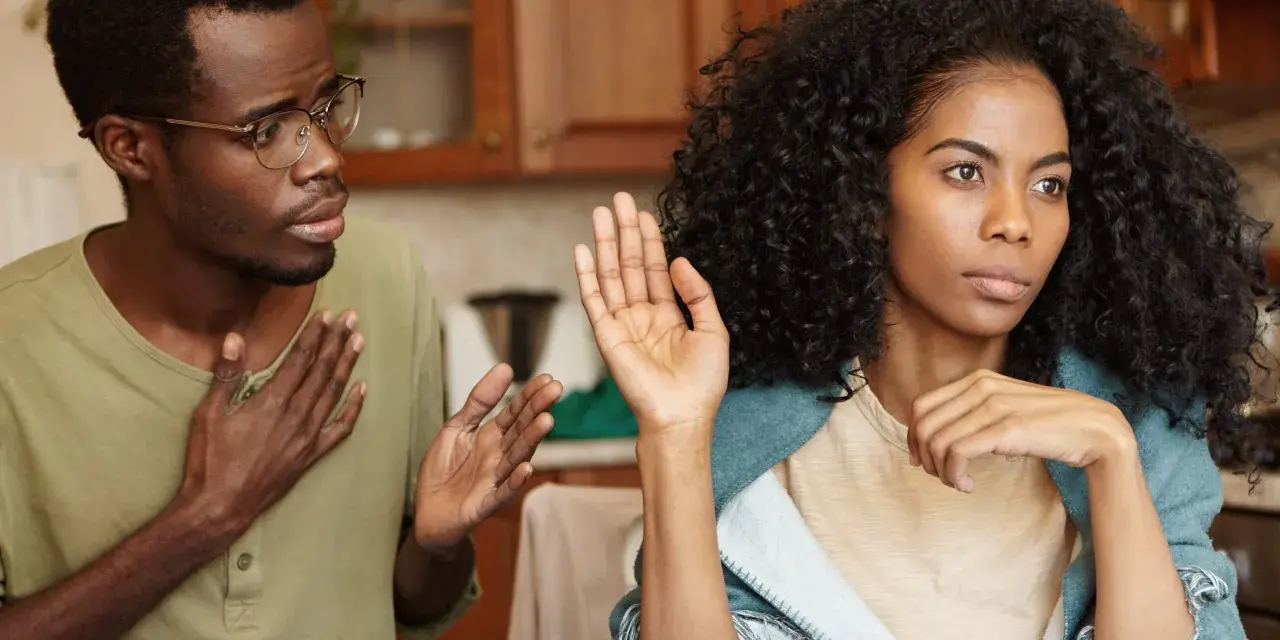 Un homme avec des lunettes parle avec passion, la main sur le cœur, tandis que sa femme, le regard ailleurs, lève une main en signe d'arrêt. Il dit : "je ne supporte plus ma femme.