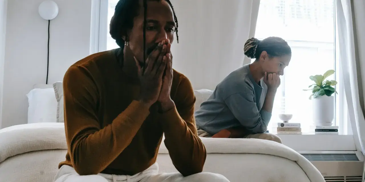Un couple traverse une crise, visiblement préoccupés, assis séparément dans une chambre lumineuse.