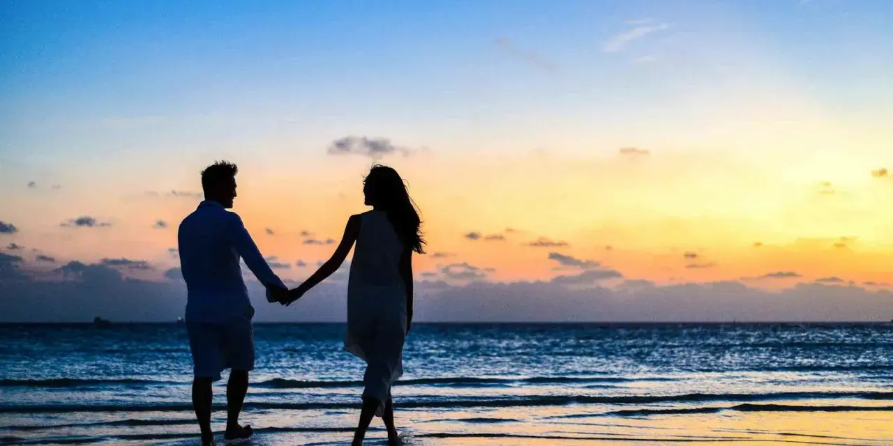 Silhouettes d'un couple se tenant la main sur une plage au coucher du soleil. Il tient à moi mais n'est pas amoureux, juste un ami.