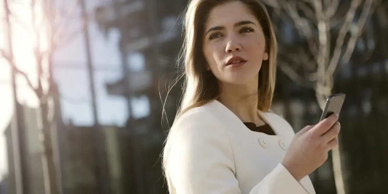 Une femme en manteau blanc tient un téléphone, prête à challenger un homme par sms.