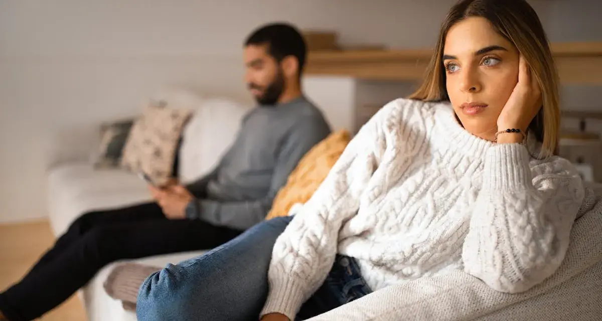 Un couple s'ennuie dans son couple, chacun absorbé par son téléphone sur le canapé, le regard perdu dans le vide.