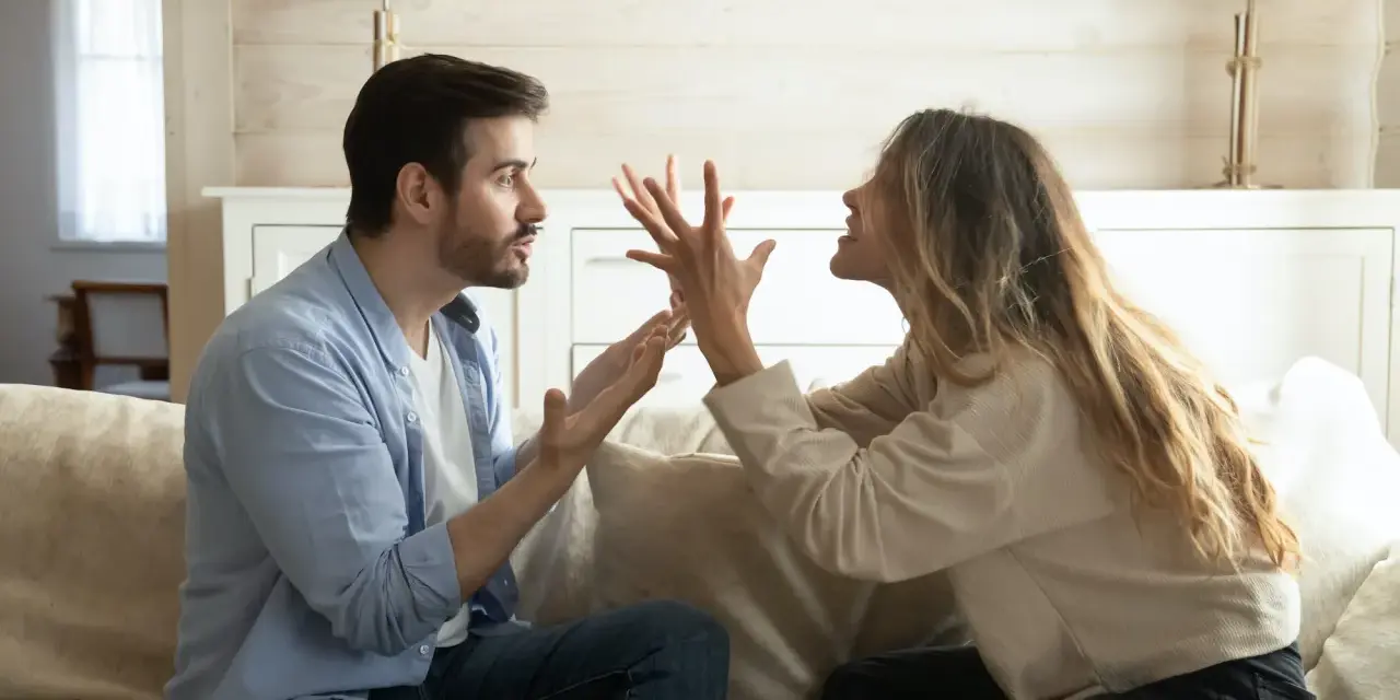 Un couple se dispute sur un canapé. L'homme semble frustré, peut-être parce qu'il est jaloux.