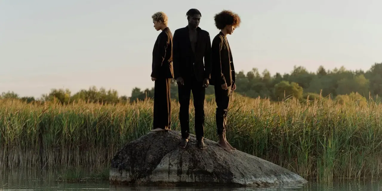 Trois personnes en noir, sur un rocher au milieu de l'eau, symbolisant la non monogamie éthique et la liberté de choix.