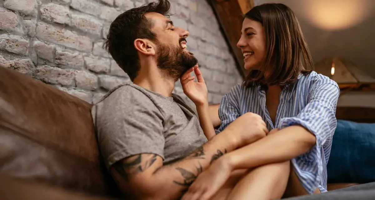 Un couple rit et se regarde tendrement sur un canapé. Le vrai amour, c'est cette complicité.