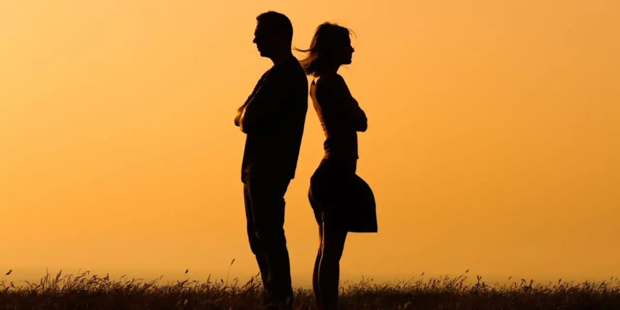 Silhouettes d'un homme et d'une femme dos à dos, bras croisés, symbolisant la communication paradoxale dans un paysage au coucher du soleil.