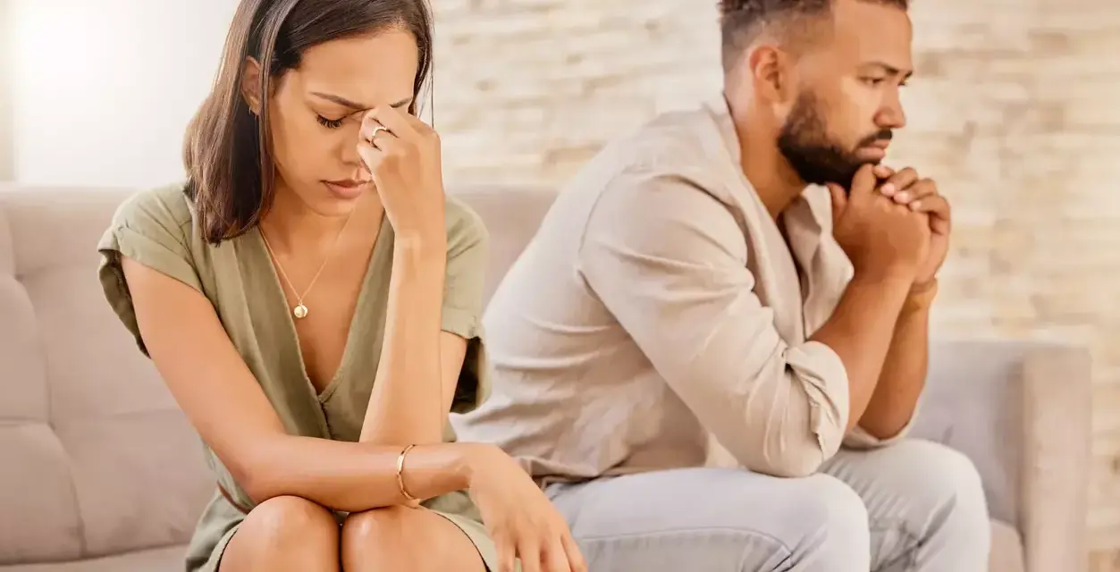 Un couple assis dos à dos, visiblement affecté par des disputes incessantes. La femme se tient la tête, l'air accablé, tandis que l'homme fixe le vide, les mains jointes.