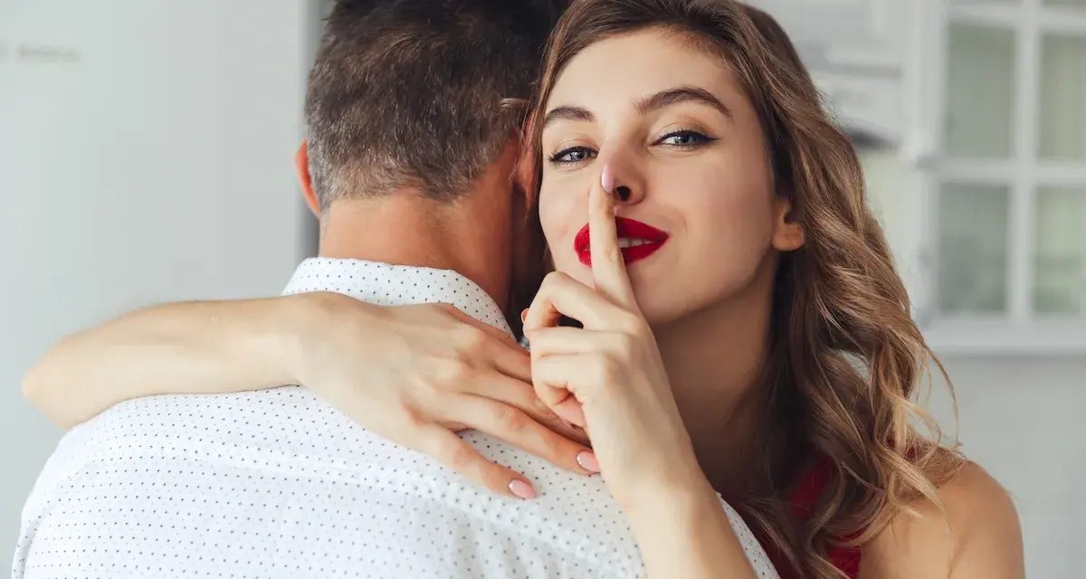 Une femme aux lèvres rouges fait signe de se taire en serrant un homme dans ses bras. Elle sait comment chauffer un mec.
