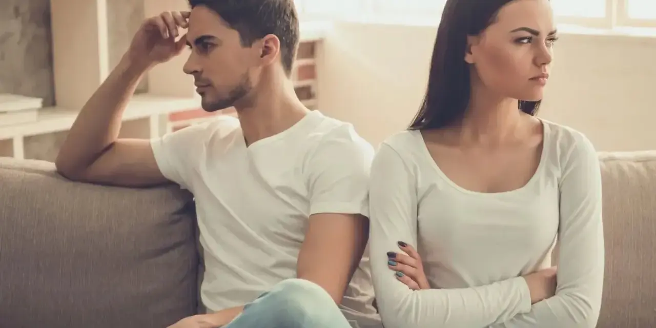 Un couple assis sur un canapé, dos à dos, visiblement en conflit. Elle croise les bras, l'air contrarié, comme s'il la prenait pour acquise.