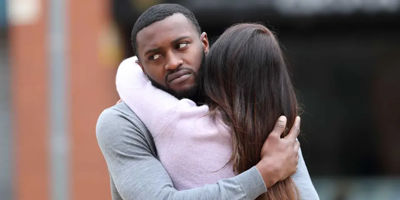 Un homme étreint une femme, mais son regard trahit des signes qu'il parle à une autre.