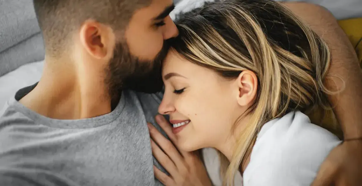Un homme embrasse le front d'une femme endormie, un moment de tendresse calin amoureux.
