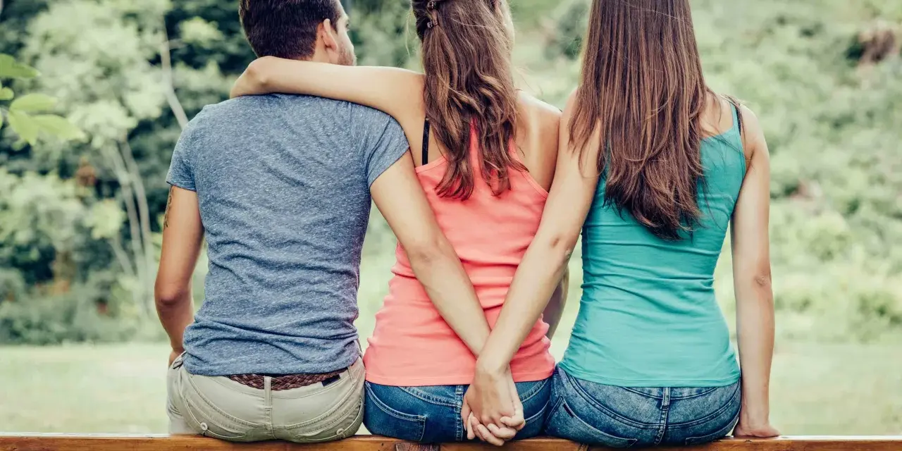 Trois personnes assises sur un banc, un homme entre deux femmes. Les mains des femmes se serrent derrière le dos de l'homme. Je ne le trouve pas beau mais il m'attire.