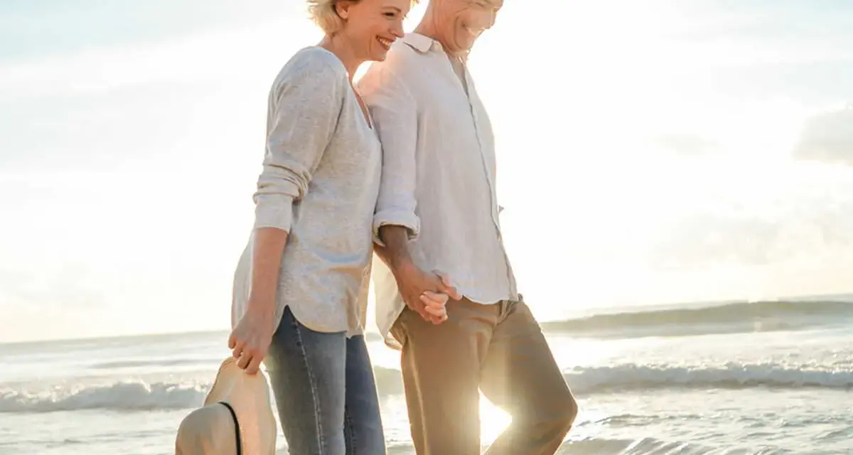 Un couple profite d'un rendez-vous amoureux sur la plage, main dans la main, au coucher du soleil.