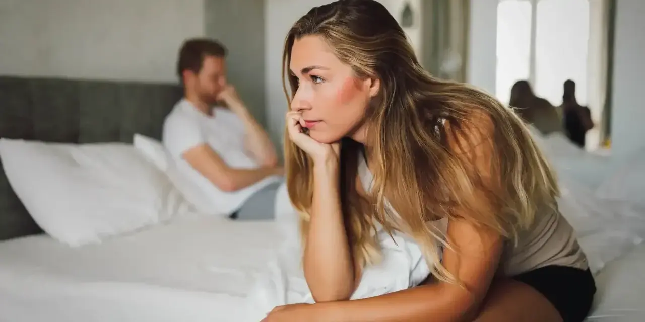 Une femme songeuse sur un lit, son mari distant en arrière-plan. Elle se demande si mon mari n'a plus envie de moi.