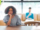 Une jeune femme songeuse, le menton appuyé sur la main, semble réfléchir à un **problème de couple à qui en parler**. Son compagnon est flou en arrière-plan.