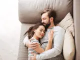 Un couple dort paisiblement sur un canapé. L'homme enlace la femme, une scène qui peut évoquer une baisse de libido chez l'homme, mais aussi un profond sentiment de sécurité et d'amour partagé.
