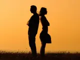 Silhouettes d'un homme et d'une femme dos à dos, bras croisés, symbolisant la communication paradoxale dans un paysage au coucher du soleil.