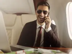 Un homme d'affaires souriant, lunettes de soleil, au téléphone dans un jet privé. Il semble rencontrer un homme riche pour conclure un accord.