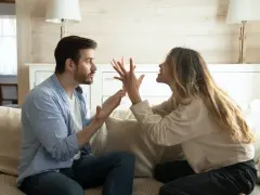 Un couple se dispute sur un canapé. L'homme semble frustré, peut-être parce qu'il est jaloux.