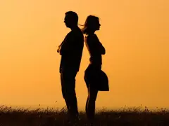 Silhouettes d'un homme et d'une femme dos à dos, bras croisés, symbolisant la communication paradoxale dans un paysage au coucher du soleil.