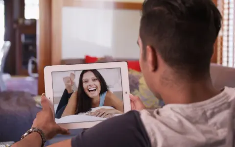 Un homme en relation à distance profite d'un appel vidéo avec sa compagne, dont le sourire illumine l'écran de sa tablette.