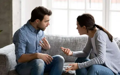 Un couple discute sur un canapé, les mains tendues, peut-être lors d'une séance de thérapie de couple pour améliorer leur communication.